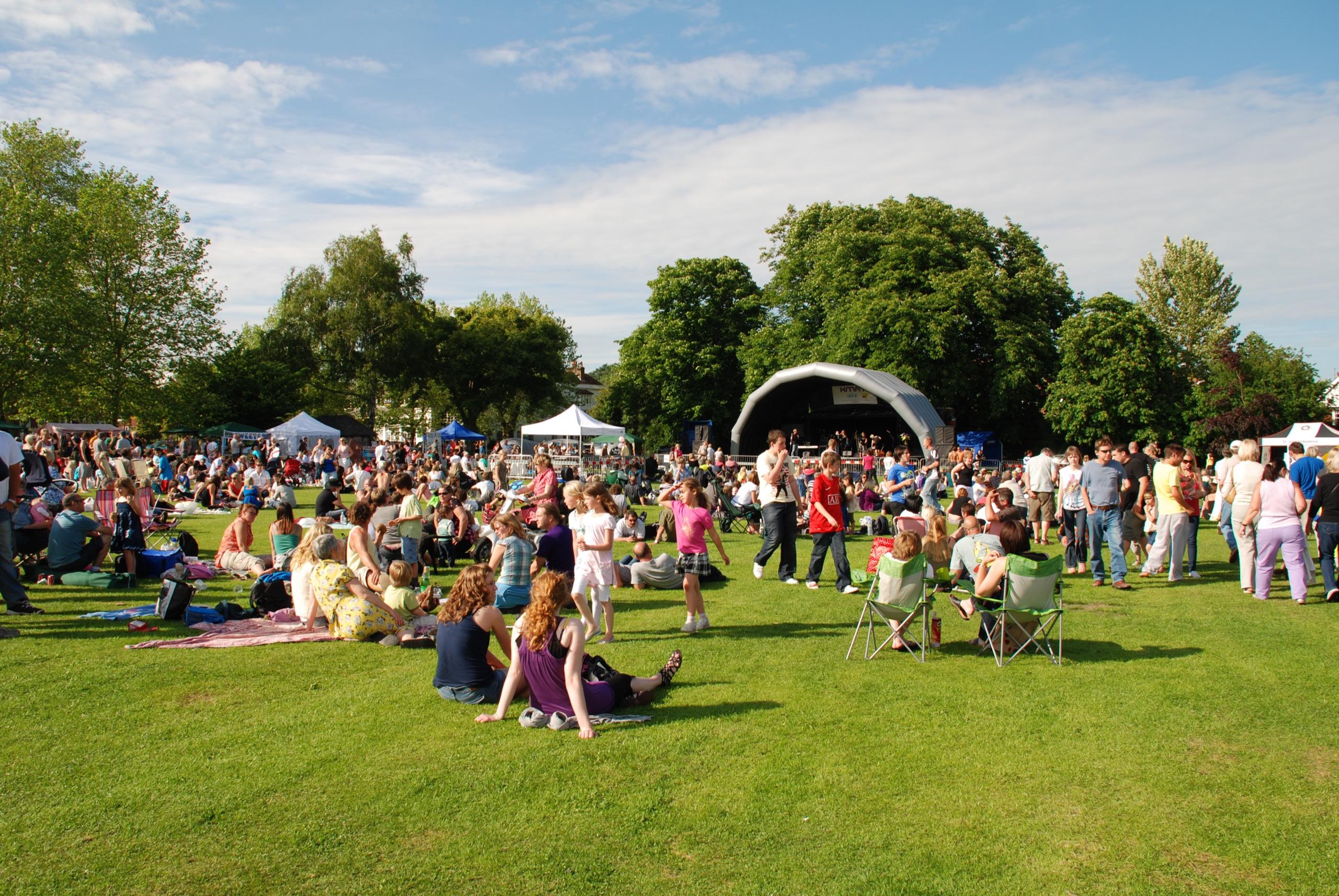 A large outdoor gathering of people enjoying a community event, likely in a park, representing diverse groups in a public setting.